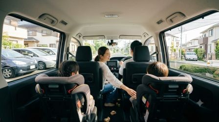保育園へ子どもを送る家族のイメージ写真。 明るい朝の自然光、住宅街の中を車で送迎している様子。