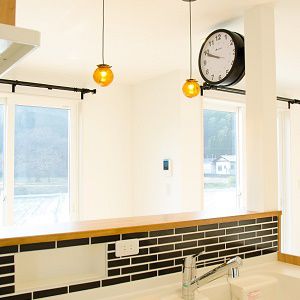キッチンの上に黒いタイル、そしてダブルフェイスの黒い時計、ヴィンテージ感をアクセントとして盛り込みながらも、白い人造大理石のキッチン天板や柱で重くなりすぎないように工夫しています。